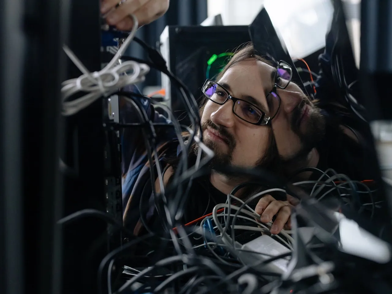IT-Administrator zwischen Kabeln hinter einem Rechner